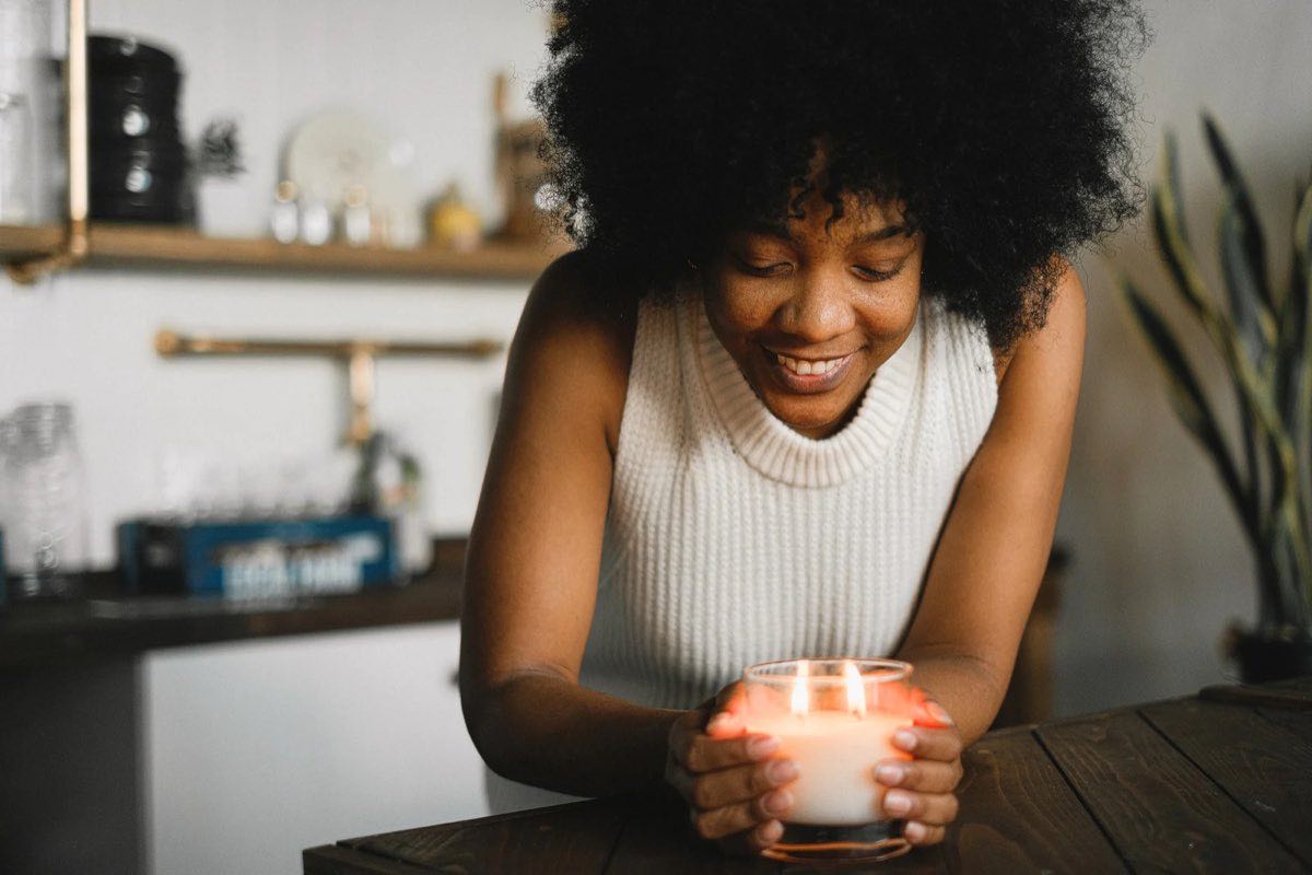 Black woman smiling while holding a lit candle in a cozy kitchen.